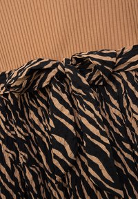 Ein Gürtel mit schwarz-braunem Zebra-Print-Muster, der an einem gerippten braunen Stoffkleidungsstück befestigt ist.