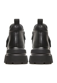 Bottines en cuir noir avec une finition texturée, dotées d'une semelle épaisse noire et d'une fermeture éclair sur les côtés.