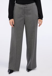 Šedé vzorované kalhoty s širokým střihem, s plochým pasem a zapínáním na knoflík, doplněné o špičaté černé boty.