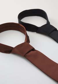 Deux cravates : l'une en brun profond et l'autre en noir uni. Les deux présentent une texture lisse et un design classique avec un détail de nœud.