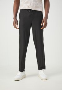Black, ribbed, drawstring pants with a relaxed fit, paired with white sneakers. Smooth texture, clean design, suitable for casual wear.