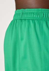 Grønne atletiske shorts med elastisk talje, med struktureret stof og detaljer langs siderne for forbedret pasform og komfort.