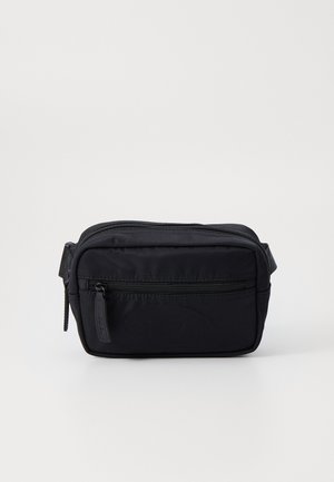Sac en nylon noir en bandoulière avec une forme rectangulaire, doté d'une poche zippée à l'avant et d'une texture douce. Comprend une poignée latérale pour un transport facile.