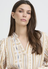 Blouse légère à motifs présentant des rayures verticales jaunes, blanches et noires. Design en V avec manches bouffantes et accents géométriques.