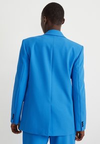 Blazer bleu sur mesure avec un revers cranté, une fente simple et des poignets boutonnés, confectionné dans un tissu lisse et structuré.