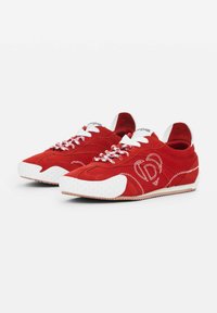 Rote Wildledersneaker mit weißen Akzenten, runden Schnürsenkeln und strukturierten Gummisohlen. Merkmale sind auffällige Nähte und ein Logodetail an der Seite.
