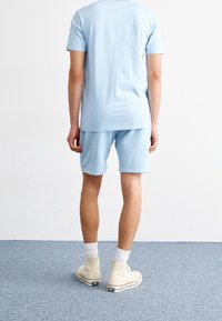 Ensemble t-shirt et short en coton bleu clair. Le t-shirt présente une coupe décontractée avec des manches courtes ; le short arrive au-dessus du genou. Chaussures montantes blanches.