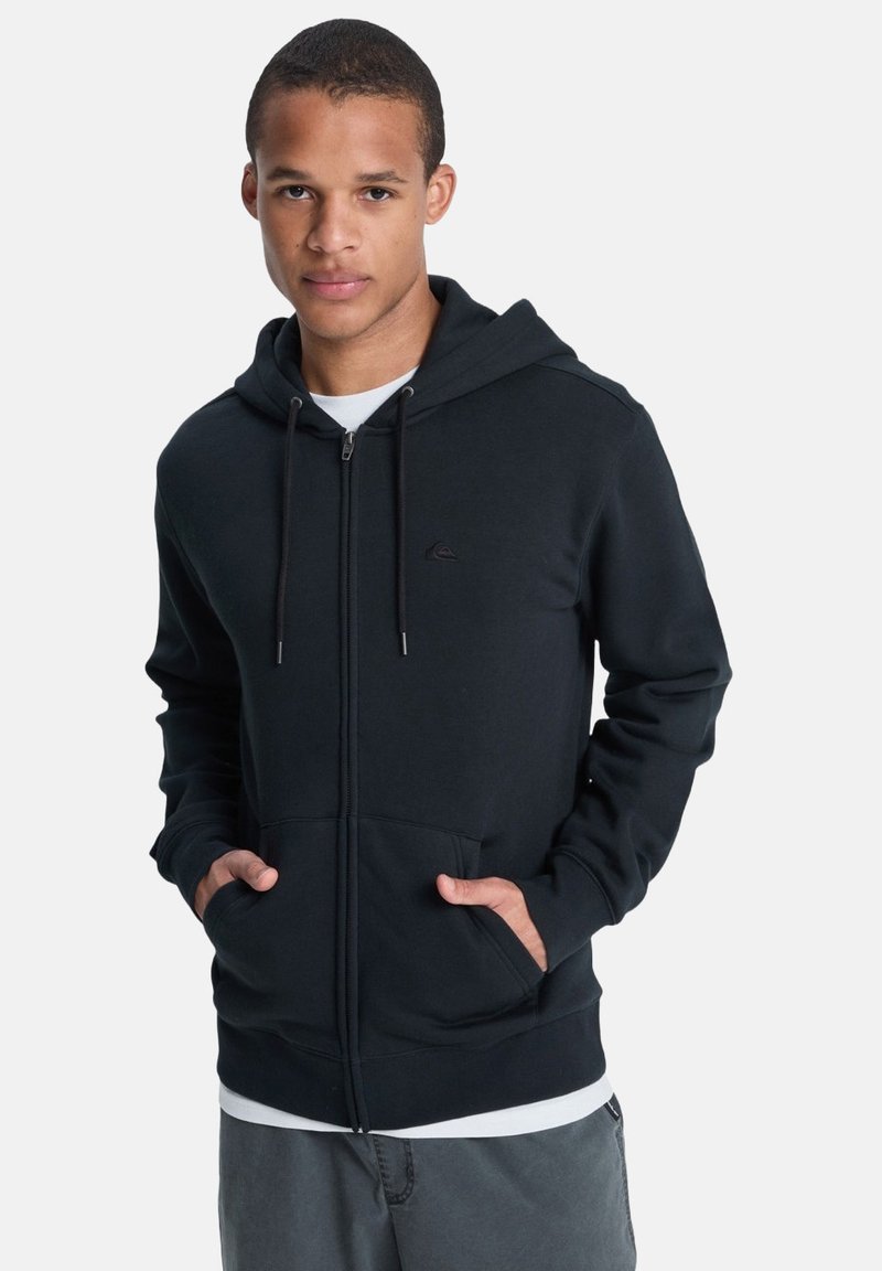 Schwarze Zip-Hoodie aus weichem Stoff, ausgestattet mit einer vorderen Tasche, verstellbaren Kordeln und einem kleinen Logo auf der linken Brust.