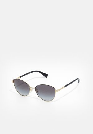 Gafas de sol de ojo de gato con montura de metal dorado, lentes grises en degradado, brazos de plástico negro y acentos decorativos en la montura.