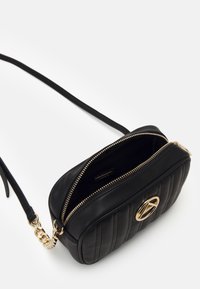 Borsa a tracolla in pelle nera con design trapuntato, hardware dorato e chiusura con zip. Presenta una tracolla regolabile e un accento con logo.