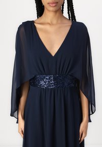 Navy blue dress with a deep V-neck, flowy cape sleeves, and a sequin-embellished waistband. Made from lightweight fabric.