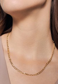 Złoty łańcuszek na szyję z wydłużonymi ogniwami o polerowanej powierzchni, spoczywający na szyi. Gładka faktura i subtelny blask.