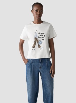 Woman wearing white T-shirt with illustration of a walking figure in leopard pants and text "all you need is love or leo," paired with blue jeans.