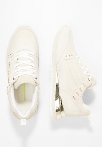 Baskets en suède beige avec des lacets blancs, accents métalliques dorés, détails cloutés sur les côtés et une épaisse semelle blanche.