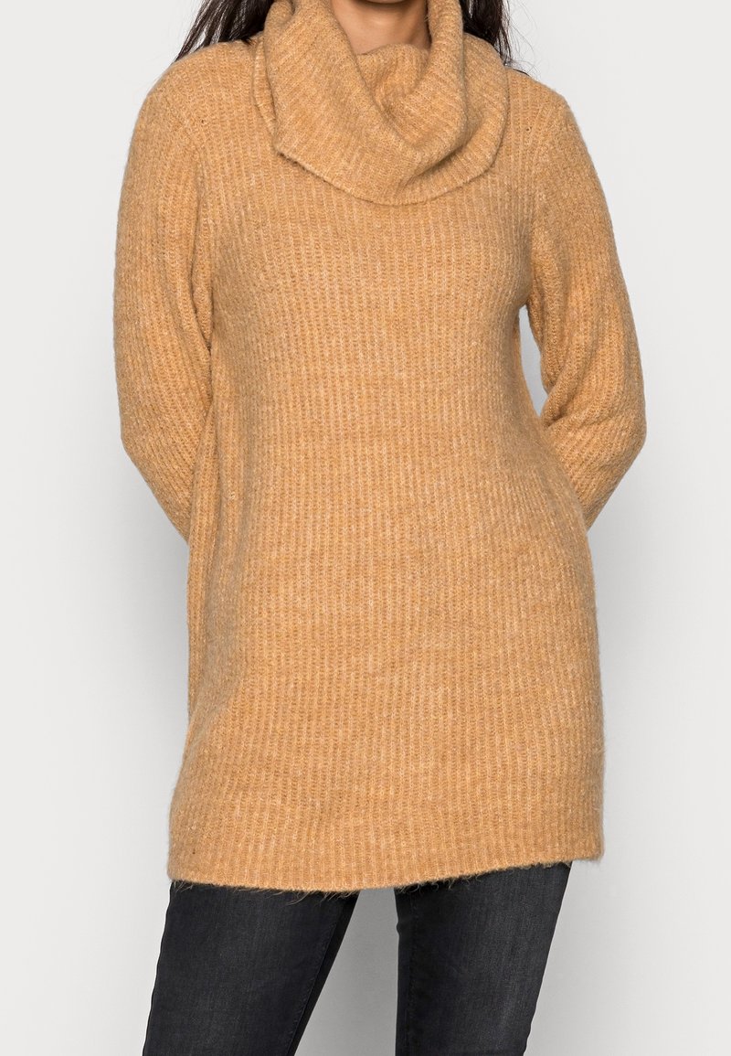 Maglione a collo a scialle in tessuto a costine marrone chiaro, con maniche lunghe e vestibilità comoda, abbinato a jeans scuri.