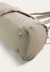 Harmaa pehmustettu olkalaukku, jossa on sileä pinta, pyöreä muoto ja kaksoisnapit sivuilla; varustettu säädettävällä hihnalla ja vetoketjulla.