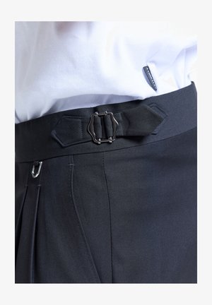 Biała koszula włożona w czarne spodnie z ozdobnym małym metalowym klamrą i paskiem przy talii.