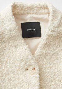 Gestructureerde off-white jas van een zachte, pluizige stof. Heeft een klassieke kraag en een enkele knoopsluiting. Etiket zegt "someday."