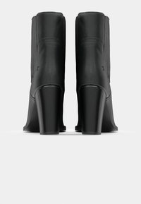 Bottines noires en cuir lisse, talons carrés incurvés, coutures verticales sur les côtés et bout arrondi.