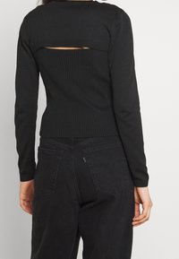 Pull noir à rayures avec des manches longues et un détail découpé horizontal à l'arrière. Design ajusté avec des manches texturées et un ourlet inférieur.