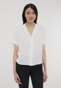 Blusa bianca a maniche corte con colletto e chiusura a bottoni, realizzata in tessuto leggero, con maniche arrotolate e una vestibilità rilassata.