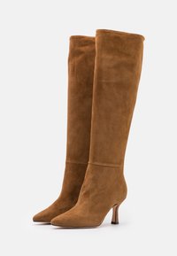 Braune Wildleder-Stiefel bis zum Knie mit spitzen Zehen und schlanken hohen Absätzen, nebeneinander auf einem weißen Hintergrund positioniert.