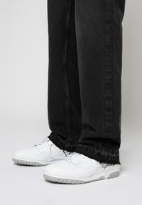 Zapatillas deportivas blancas con una superficie texturizada, combinadas con unos vaqueros negros con dobladillos deshilachados y corte recto.