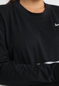 Sweatshirt noir à manches longues avec un col ras du cou, arborant un logo Nike gris sur la poitrine et une texture de tissu lisse et douce.