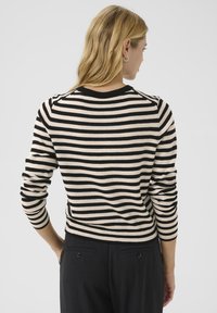 Pull rayé noir et beige avec des manches longues et un col rond, doté d'un tissu texturé et d'une silhouette ajustée.