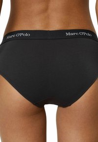 Slip in cotone nero con design uniforme, caratterizzato da un ampio elastico in vita con la scritta "Marc O'Polo" in lettere bianche. Tessuto liscio, taglio a vita bassa.