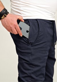 Navy Jogginghosen mit glatter Textur, ausgestattet mit einer seitlichen Tasche, die ein Smartphone sicher hält. Verstellbarer Kordelzugbund.
