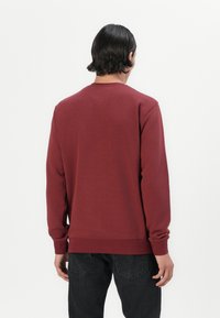 Maroon sweatshirt with long sleeves, crew neck, and ribbed cuffs. Made of soft, textured fabric, displaying a simple, solid design.