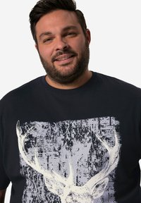 Námořnická modrá tričko vyrobené z bavlny, s bílou grafikou jeleních rohů a opotřebovanou texturou ve středu. Kulatý výstřih.