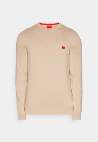 Pull beige à manches longues, col rond, avec poignets et ourlet côtelés, orné d’un petit écusson rouge du logo Hugo sur la poitrine et d’une étiquette rouge au col.