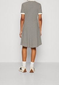 Černo-bílé pruhované šaty s krátkými rukávy, kulatým límcem a rozšířeným lemem. Doplněno bílými ponožkami a volnočasovými teniskami.