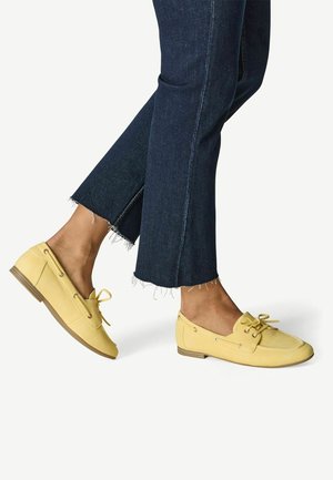 Chaussures jaunes à enfiler avec lacets, en cuir lisse. Profil bas avec un bout arrondi et une semelle marron texturée. Pantalon court en denim.