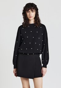 Felpa nera a maniche lunghe con decorazioni di perle bianche, abbinata a una gonna nera a portafoglio. Tessuto morbido, vestibilità comoda e spalle scese.