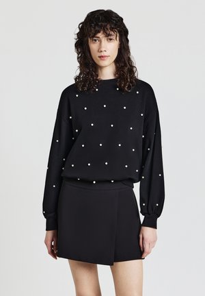 Felpa nera a maniche lunghe con decorazioni di perle bianche, abbinata a una gonna nera a portafoglio. Tessuto morbido, vestibilità comoda e spalle scese.