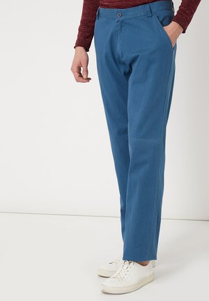 Pantalones de algodón azul con un corte recto, que cuentan con bolsillos frontales y cierre de botón, combinados con zapatillas blancas. Textura suave.