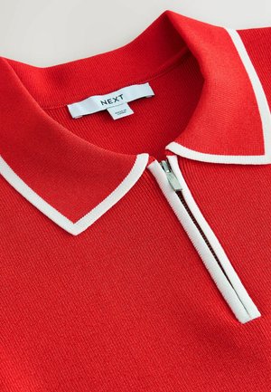 Rotes Strick-Poloshirt mit kontrastierendem weißem Kragen, ausgestattet mit einem kurzen Reißverschluss vorne und einem Etikett mit der Aufschrift "NEXT." Texturiertes Gewebe.