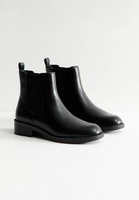 Botas de cuero negro hasta el tobillo con paneles laterales elásticos, punta redondeada y tacones bajos en bloque. Presentan tiradores en la parte posterior para facilitar su uso.