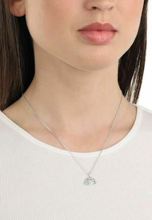 Collar de plata con un colgante de flor de loto en una cadena fina, llevado por una persona con una blusa de ribetes claros, primer plano del cuello y la cara.
