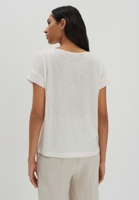 Weißes Ripp-T-Shirt mit kurzen Ärmeln, lässiger Passform und rundem Halsausschnitt, von hinten gezeigt, betont die Textur und klaren Linien.