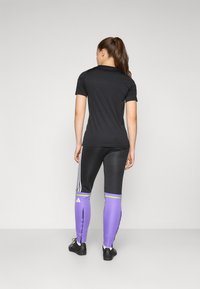 Must musta lühikese varrukaga spordipusa, millele on sobitatud sobivad mustad ja lillad legginsid, millel on valged triibud ja rohelised aktsendid.
