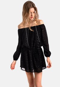Robe noire décolletée avec des manches bouffantes longues, taille cintrée et motifs floraux. La texture transparente et le tissu léger créent un effet fluide.