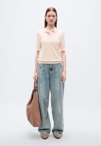 Ροζ ανοιχτό polo πουκάμισο με γιακά και κουμπιά μπροστά, σε συνδυασμό με φαρδιά, ξεθωριασμένα μπλε τζιν. Καφέ σουέντ τσάντα ώμου.