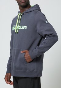 Sudadera con capucha gris hecha de tejido, con un bolsillo delantero. Presenta un cordón verde neón y texto de logo en el pecho.
