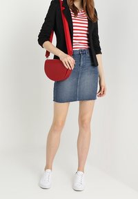Rot gestreiftes T-Shirt unter einem schwarzen Blazer, kombiniert mit einem Jeansrock und weißen Sneakers. Eine rote Umhängetasche rundet das Outfit ab.