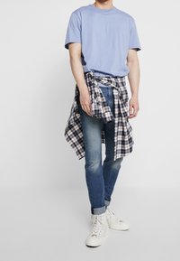 Ljusblå kortärmad t-shirt, mörkblå slim jeans och vita högskor. Lager med en rutig skjorta knuten i midjan.