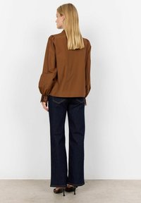 Brown long-sleeve blouse with puffed sleeves, textured lace cuffs, paired with dark denim wide-leg jeans and strappy black heels.
